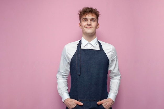Фото Портрет молодого рабочего официанта в форме и фартуке на розовом фоне