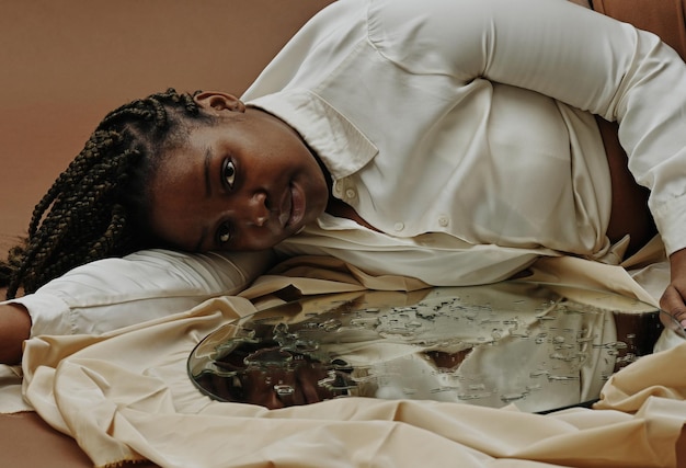 写真 表面に水滴とカメラを見て鏡の近くに横たわってアフリカの若い女性の肖像画