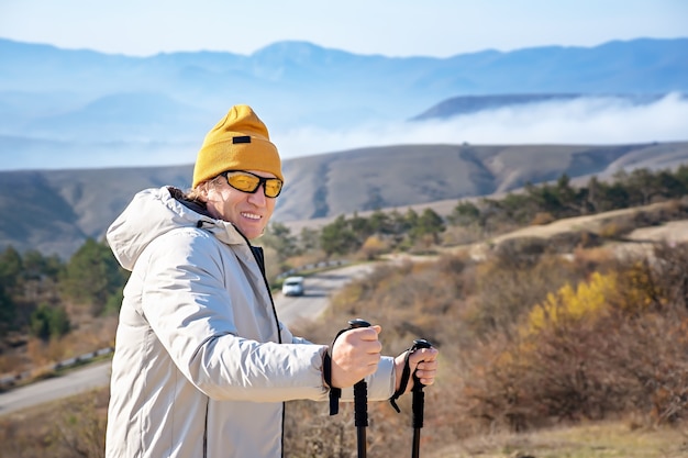 写真 山の高いところに立っているノルディックウォーキングスティックと大人の笑顔の男の肖像画。