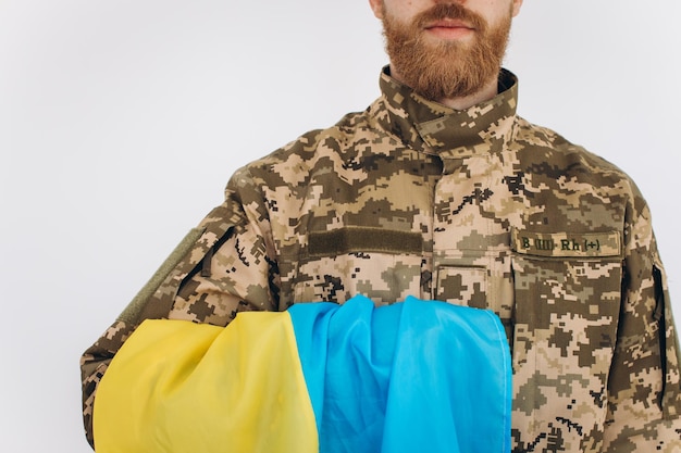 Фото Портрет эмоционального молодого бородатого украинского патриота-солдата в военной форме с флагом в офисе