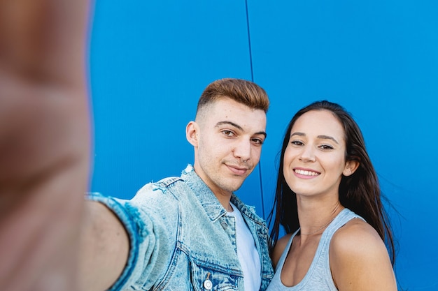 青のスマートフォンで自分撮りをしている孤立した若くて幸せなカップルの肖像画