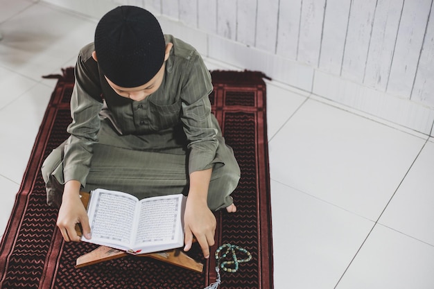 写真 伝統的な衣装を着たアジアのイスラム教徒の少年の肖像画は、聖典アルコーランを読んでいました