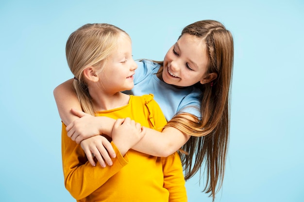 Фото Портрет привлекательных маленьких сестер, обнимающихся и смотрящих друг на друга, стоящих на синем фоне