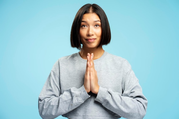 Фото Портрет привлекательной позитивной азиатской женщины христианки, молящейся, желающей чего-то, смотрящей вверх, стоящей изолированной на синем фоне.