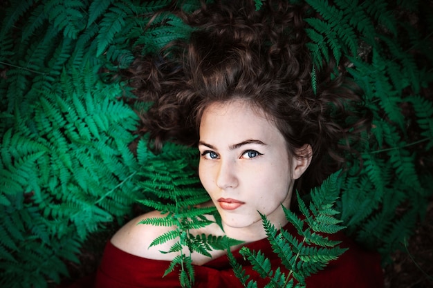 Фото Портрет красивой девушки в красном платье лежит на листьях папоротника