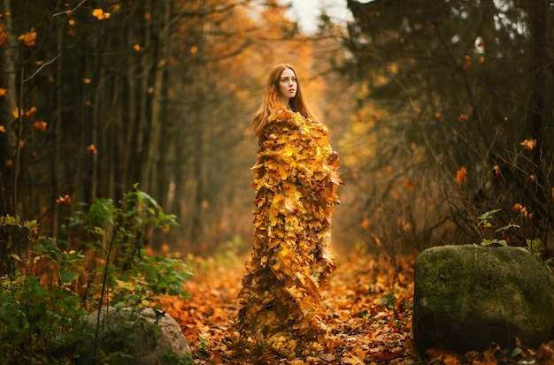 Фото Портрет красивой рыжеволосой женщины, платье из осенних листьев в осеннем парке