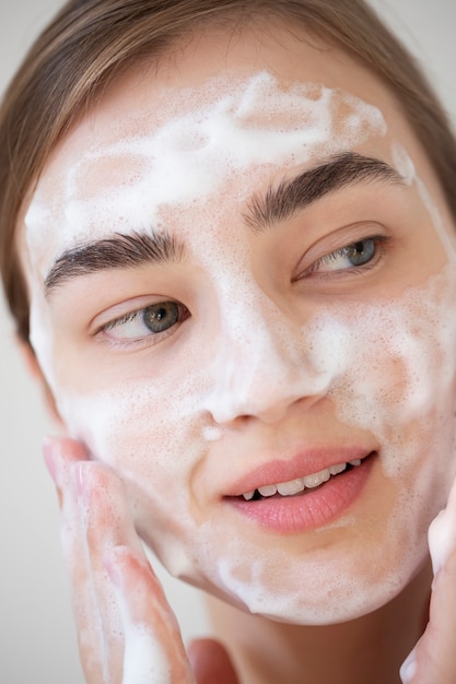 写真 フォームクレンザーで顔を洗う透明な肌を持つ美しい女性の肖像画