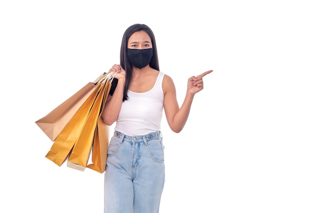 보호용 마스크를 쓰고 흰색 배경에 쇼핑백을 들고 있는 아름다운 젊은 아시아 여성의 초상화