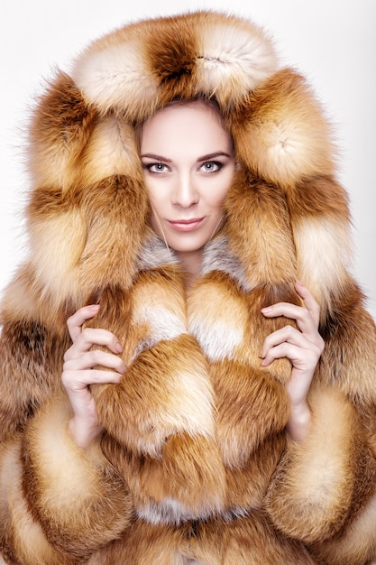 写真 豪華なキツネの毛皮のコートで美しい若いブロンドの女性の肖像画。灰色の背景に冬のファッション