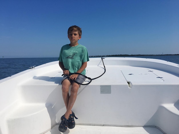 Фото Портрет мальчика, сидящего на лодке в море на чистом небе