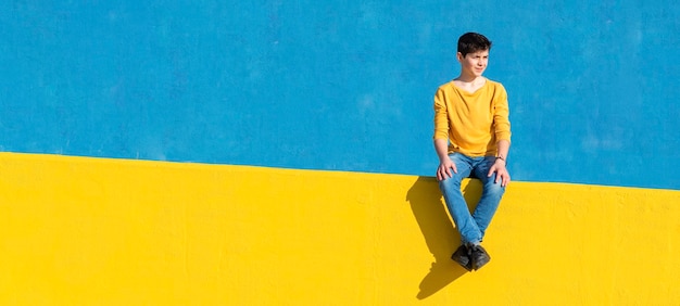 写真 青い壁の反対側の黄色いレールに座っている男の子の肖像画