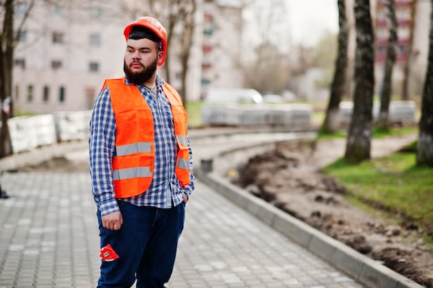 Фото Портрет жестокого бороды работник человек костюм строительный рабочий в безопасности оранжевый шлем против тротуара с рулеткой в руке.