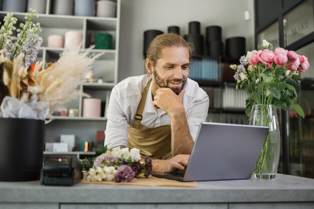 Фото Портрет кавказца-предпринимателя, сидящего в собственном цветочном магазине и печатающего на ноутбуке
