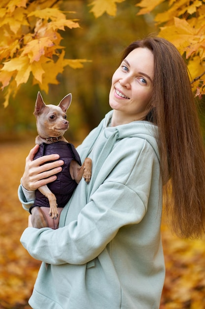 写真 秋の公園で彼女の腕に小さな犬のおもちゃのテリアと陽気な魅力的なウォーワンの肖像画