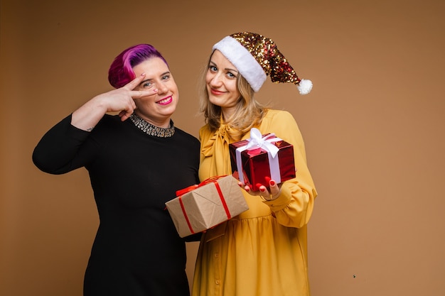 写真 クリスマスプレゼントを交換して笑顔の陽気な女性の肖像画。きらめくサンタの帽子と黄色のドレスを着ている金髪