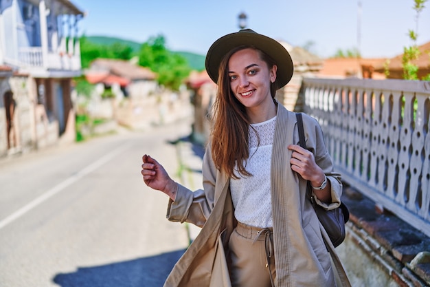 Фото Портрет милой счастливой радостной привлекательной улыбающейся идущей молодой девушки-путешественницы в шляпе и рюкзаке в яркий солнечный день