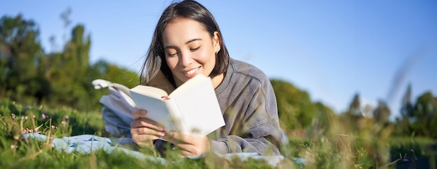 写真 草の上に横たわってお気に入りの本でリラックスして公園で読んでいる可愛い韓国人の女の子の肖像画