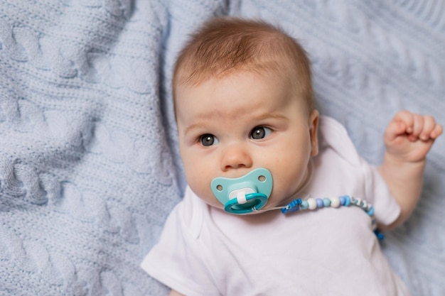 사진 파란색 니트 담요에 등을 대고 입에 젖꼭지를 물고 있는 귀여운 신생아의 초상화. 모유 수유. 행복한 어린 시절과 모성의 개념. 건강한 아이. 고품질 사진