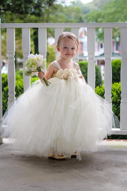 写真 白いドレスを着た可愛い笑顔の女の子の肖像画レールに花束を握っている