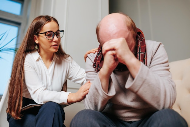 Фото Портрет депрессивного пожилого человека, плачущего во время сеанса терапии с психиатром-женщиной, пытающейся утешить его. молодой психотерапевт консультирует старика.