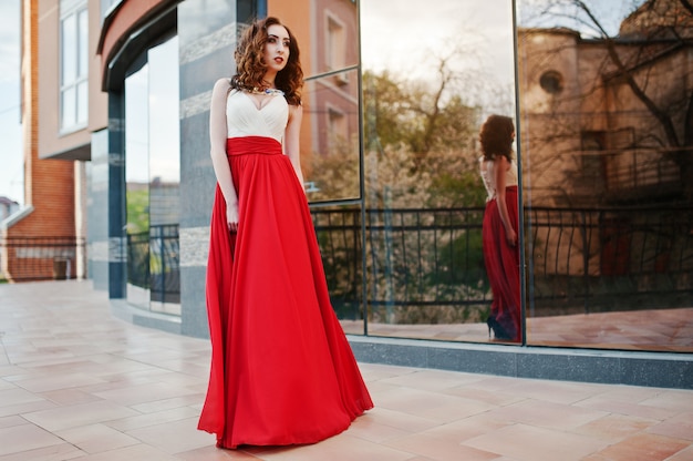 写真 赤いイブニングドレスでファッショナブルな女の子の肖像画は、モダンな建物の背景ミラーウィンドウを提起