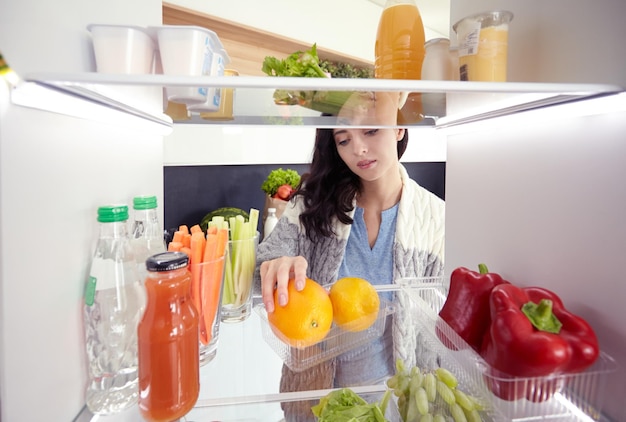 写真 健康食品の野菜や果物でいっぱいの開いた冷蔵庫の近くに立っている女性の肖像画