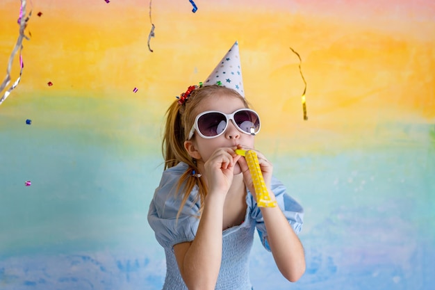 写真 黄色い背景の明るいコンフェッティと誕生日の帽子をかぶった面白い女の子の肖像画