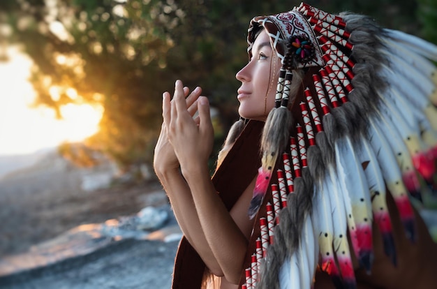 사진 해가 지는 빛 속의 자연에서 네이티브 아메리카 헤드 드레스를 입은 손을 가진 소녀의 초상