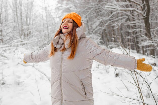 写真 幸せな美しい女の子の肖像画 若い喜びに満ちたポジティブな女性が 雪の雪花と遊んで歩いています