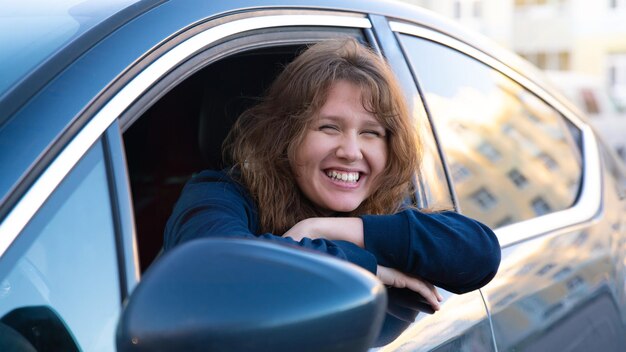 写真 幸せな肯定的な女の子の若い女性ドライバーの肖像画は彼女の車の新しい自動車に座って楽しんで運転を楽しんでいます