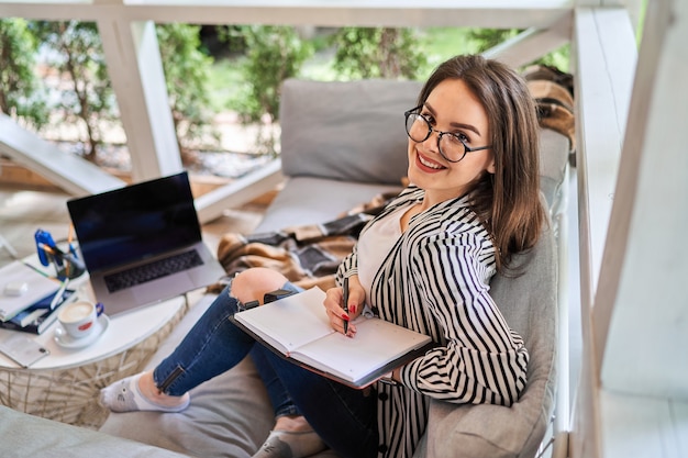 写真 ノートブックと自宅で幸せな笑顔のフリーランサーの女性の肖像画。