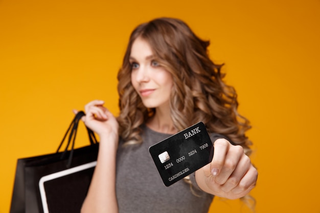 Фото Портрет счастливой молодой женщины брюнет держа кредитную карточку и хозяйственные сумки