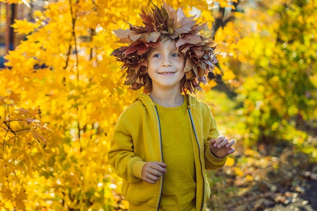 Фото Портрет маленького улыбающегося ребенка с венком из листьев на фоне головы солнечного осеннего парка.
