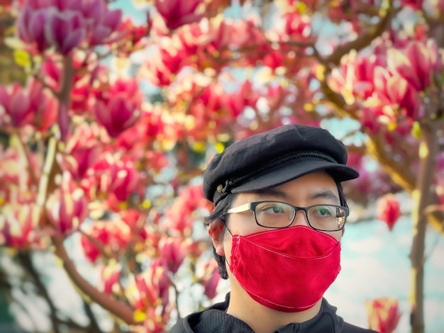 写真 ピンクの花を ⁇ かせるマグノリアの木に対して ⁇ 帽子眼鏡と顔マスクをかぶった男の肖像画