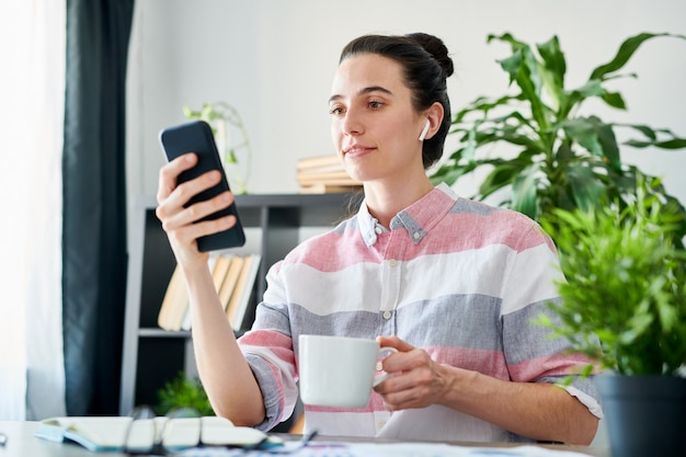 職場でスマートフォンを使用してコーヒーを飲み、コピースペースの現代の若い女性の肖像画