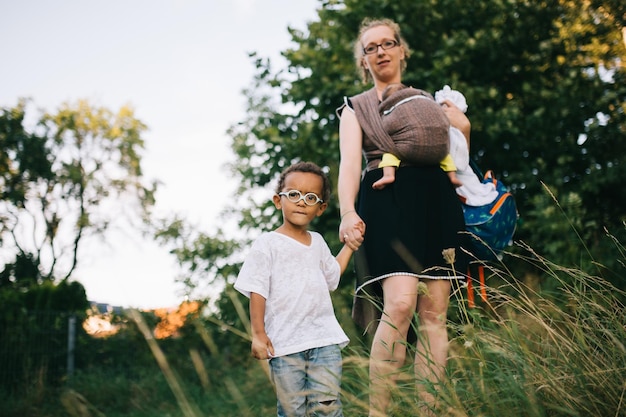 写真 樹木の向こうの畑に立っている子供たちとの母親の肖像画