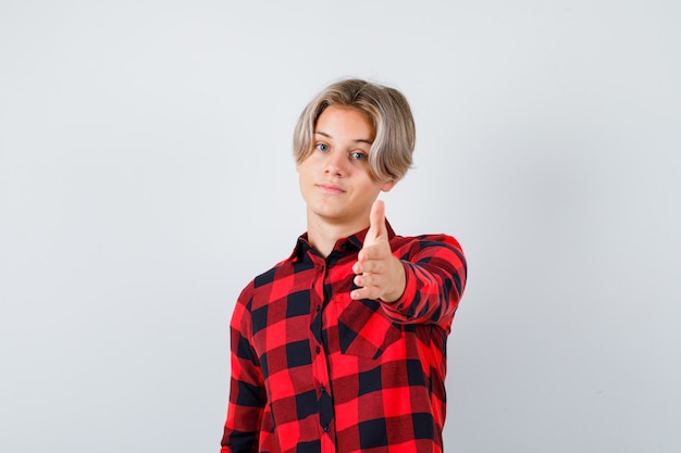 Фото Портрет симпатичного мальчика-подростка, протягивающего руку вперед в клетчатой рубашке и уверенно выглядящего спереди