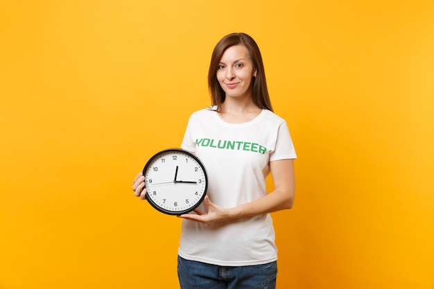 書かれた碑文の緑のタイトルボランティアと白いtシャツのきれいな女性の肖像画は、黄色の背景で隔離の時計を保持します。自主的な無料支援支援、チャリティー猶予労働時間の概念
