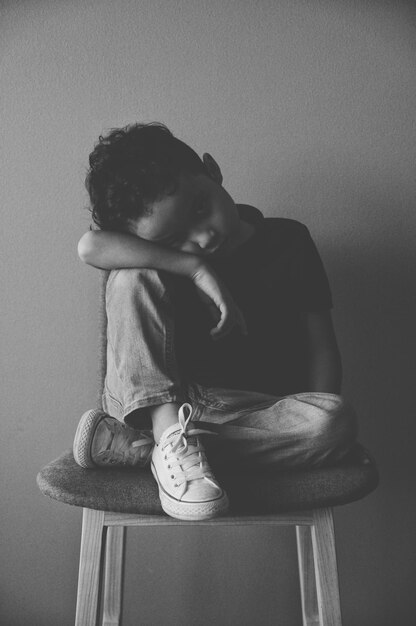 Фото Портрет грустного мальчика, сидящего на стуле у стены.