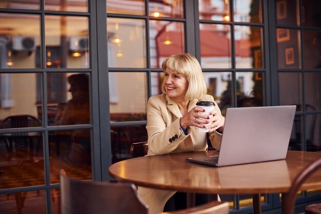 현대 노트북으로 카페에 실내에 앉아 있는 고위 여성의 초상화.