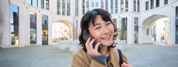 写真 携帯電話で話すアジアの笑顔の女の子のポートレートは、街を歩くスマートフォンで友人と話す