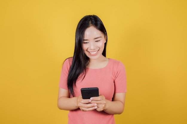 노란색 배경에 스마트폰을 사용하여 웃고 있는 아시아 여성의 초상화