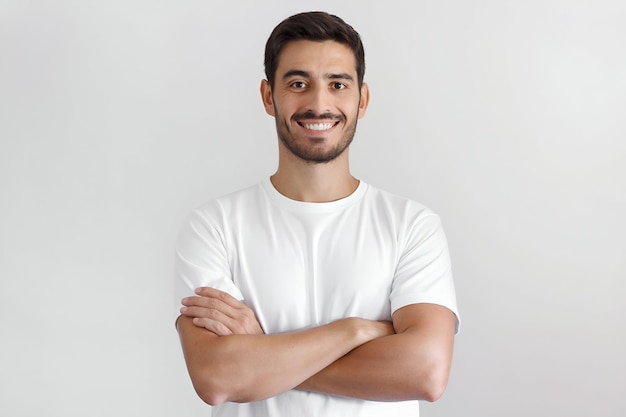 Фото Портрет улыбающегося симпатичного мужчины в белой футболке, стоящего с скрещенными руками на сером фоне