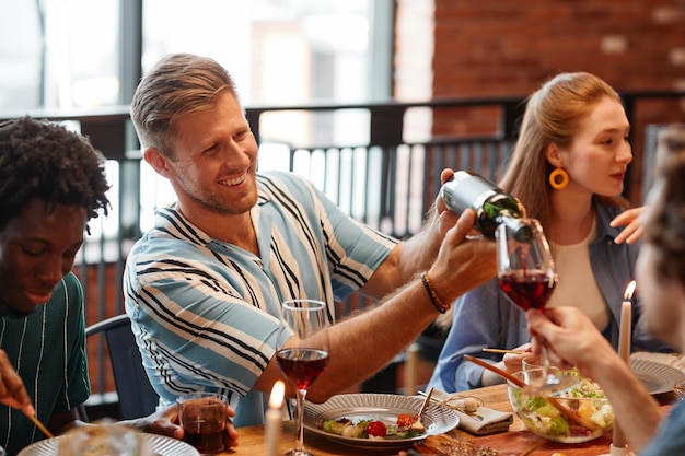 Фото Портрет улыбающегося мужчины, наливающего вино в бокал, наслаждаясь ужином с друзьями в уютной обстановке