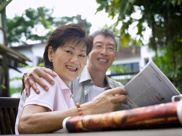 사진 뒷마당 에서 신문 을 읽는 미소 짓는 고령 부부 의 초상화