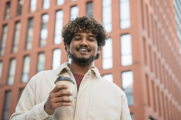 写真 屋外で一杯のコーヒーを保持している笑顔のスタイリッシュなインド人の肖像画。コーヒー ブレークのコンセプト