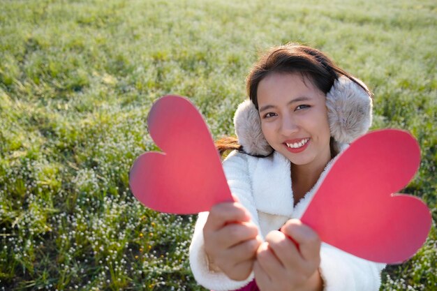 写真 植物の上に立って赤い心の形を握っている笑顔の女性の肖像画