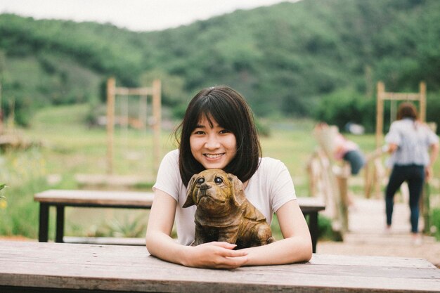 写真 ピクニックテーブルに座っている犬の像を持つ笑顔の女性の肖像画