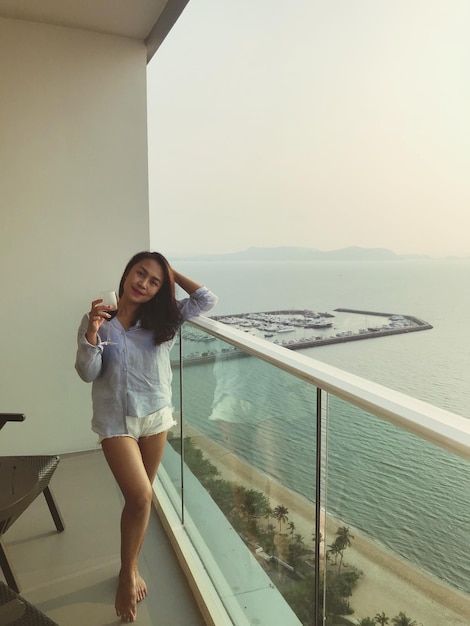 Фото Портрет улыбающейся женщины с бокалом вина, стоящей на балконе у моря