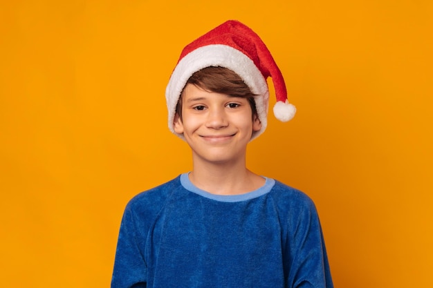 사진 노란색 배경 에 빨간 산타클로스 모자를 입은 미소 짓는 어린 소년 의 초상화